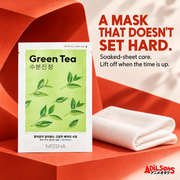 MISSHA Green Tea mask on a bold red sculptural set beside folded soft fabric.